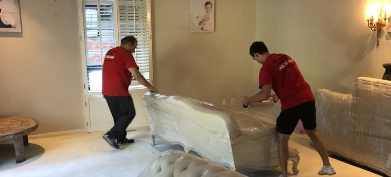 Two movers from packing and unpacking services San Francisco offers, wrapping a couch