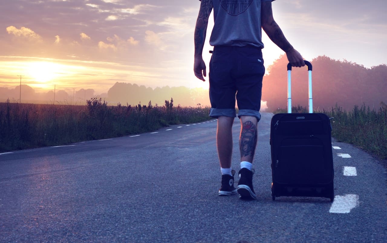 A person with luggage on the road leaving into the sunset