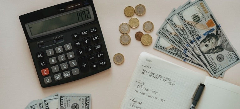 Picture of coins and money next to a calculator and a notebook 