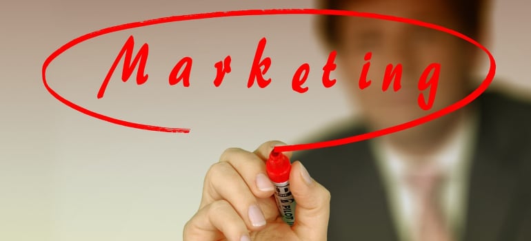 A person writing the word marketing using a marker